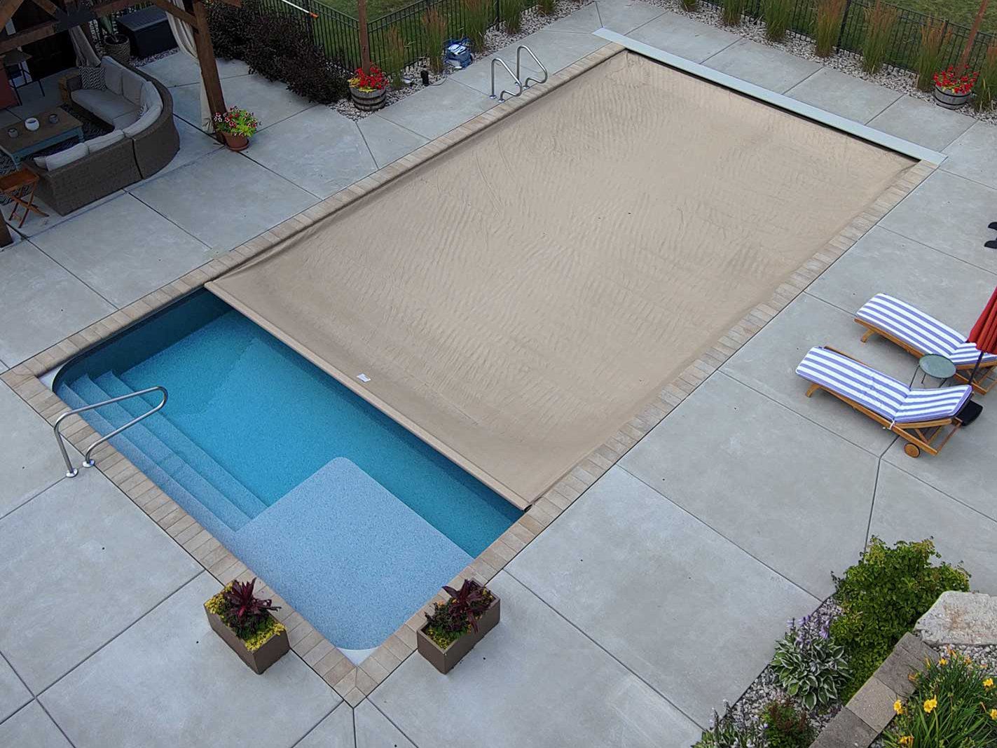 Mostly closed Coverstar Atom automatic pool cover on fiberglass pool surrounded by nicely desgned concrete patio.