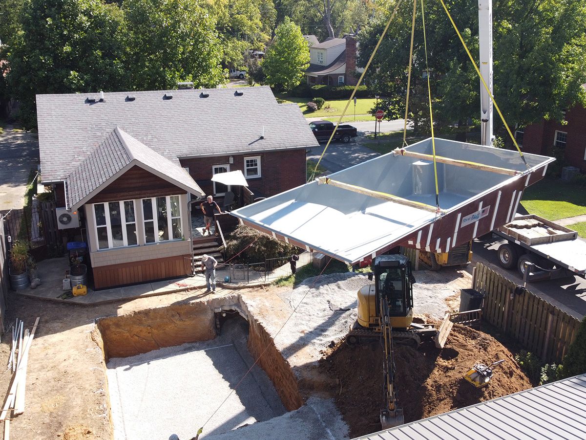 Moving fiberglass pool into place with a crane during installation.