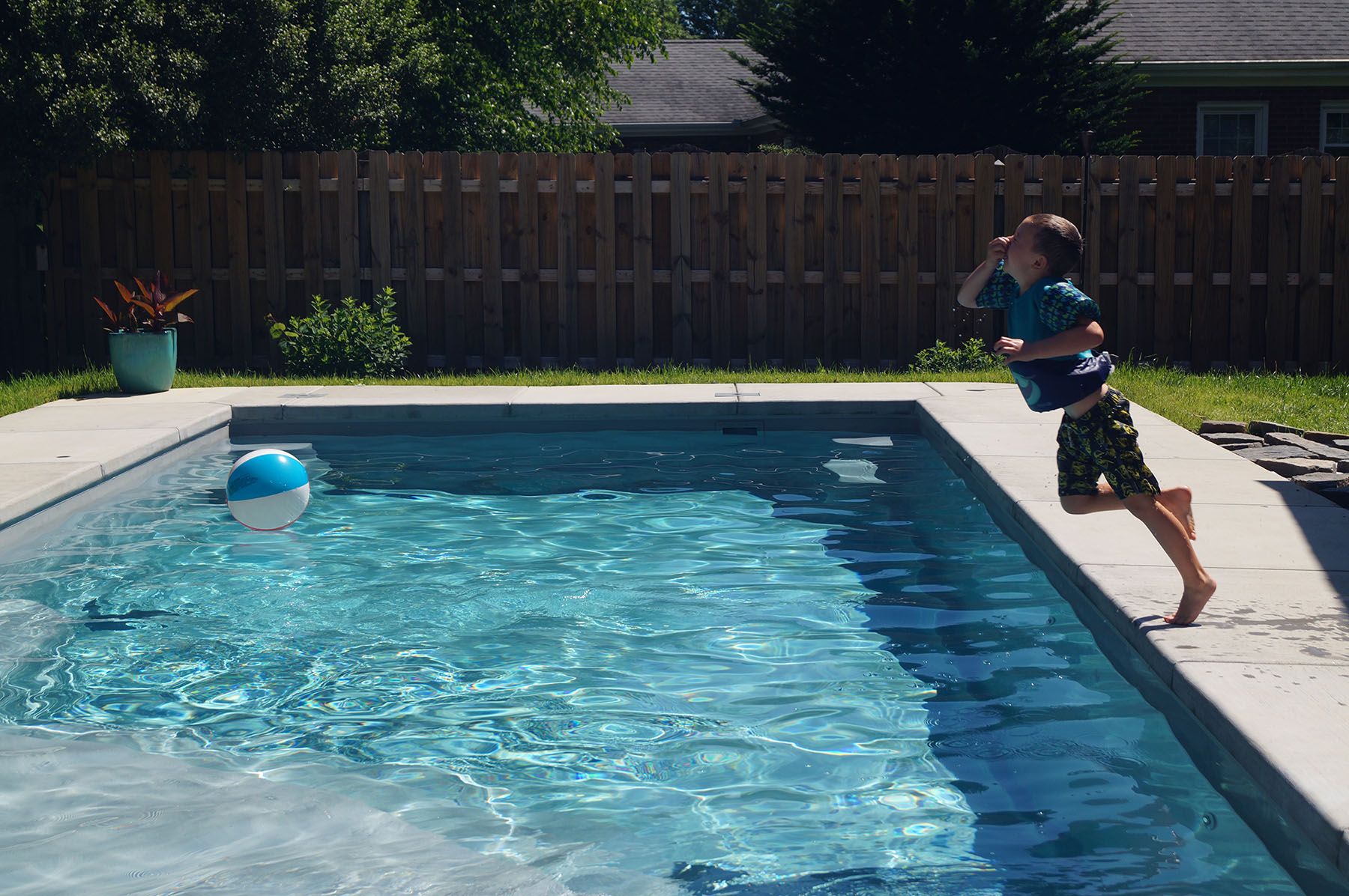 Young boy holding his nose and jumping in to an in-ground fiberglass pool on a sunny day in Louisville, Kentucky.
