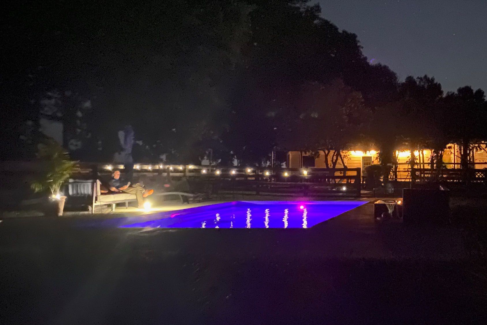 Rectangular in-ground fiberglass swimming pool in a nicely landscaped backyard in Prospect, Kentucky at night with dramatic lighting.