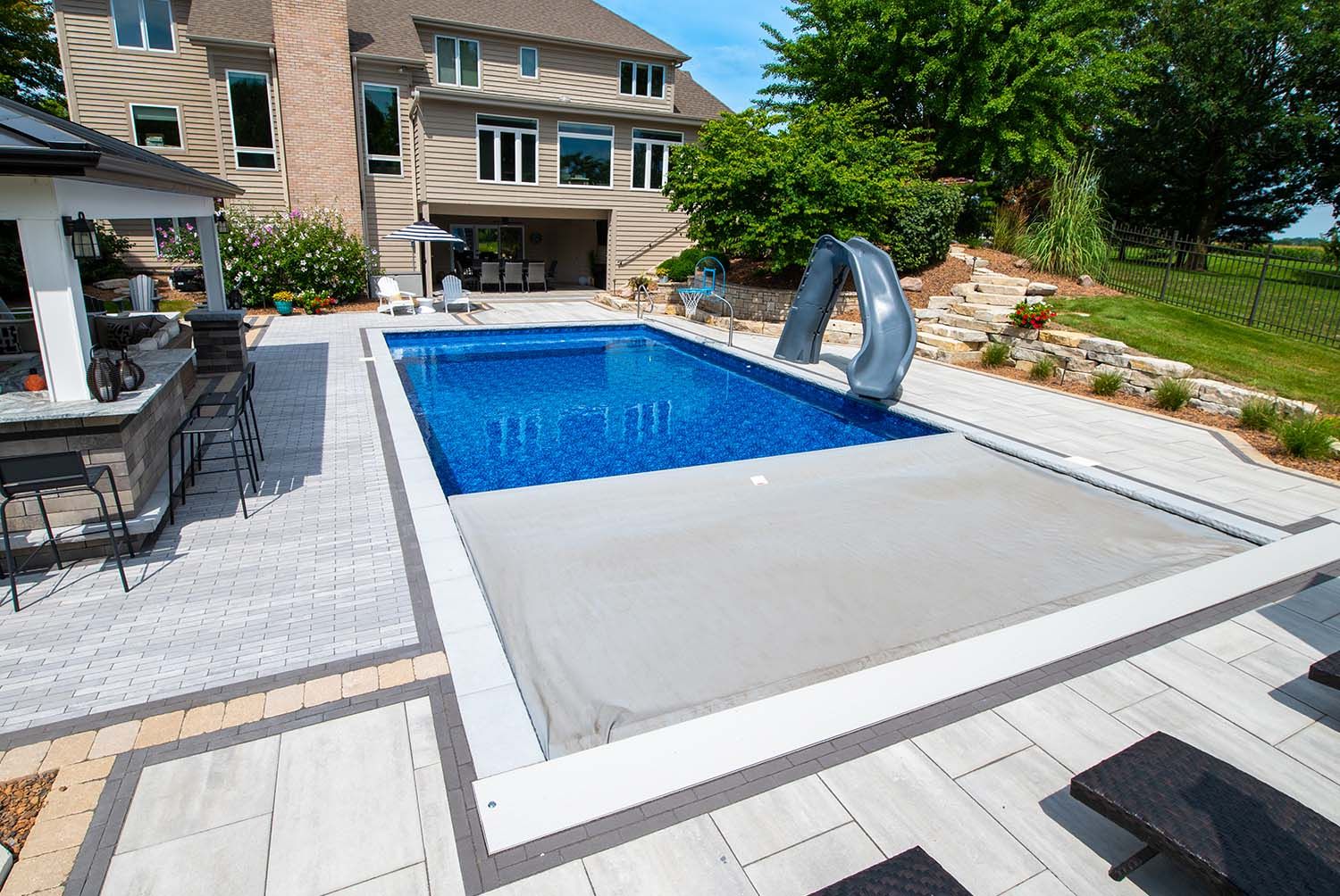 Partially open Coverstar CS300HD automatic pool cover on a rectangular fiberglass pool in a nice backyard with a concrete patio.