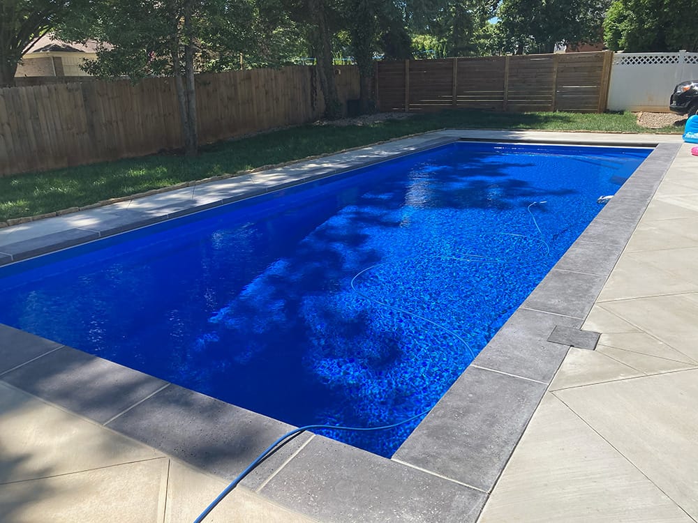 Deep blue in-ground rectangular fiberglass pool with nice concrete patio in backyard with wooden privacy fence in Louisville, Kentucky.