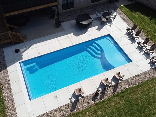 Aerial view of a rectangular in-ground fiberglass pool with a nice concrete patio and outdoor chairs in Louisville, Kentucky.