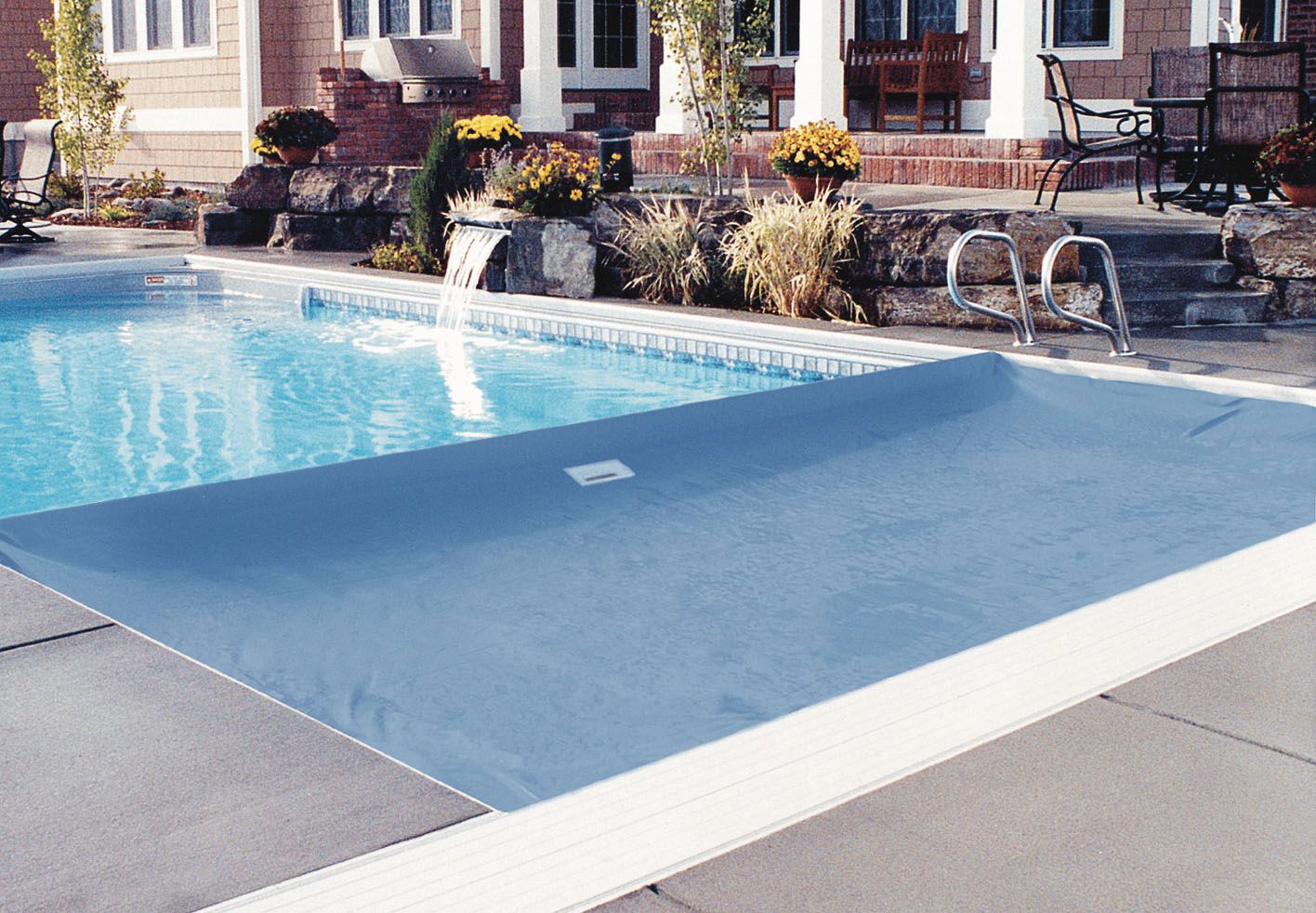 Coverstar CS3000 automatic pool cover on an in-ground fiberglass pool with a small waterfall and decorative landscaping.