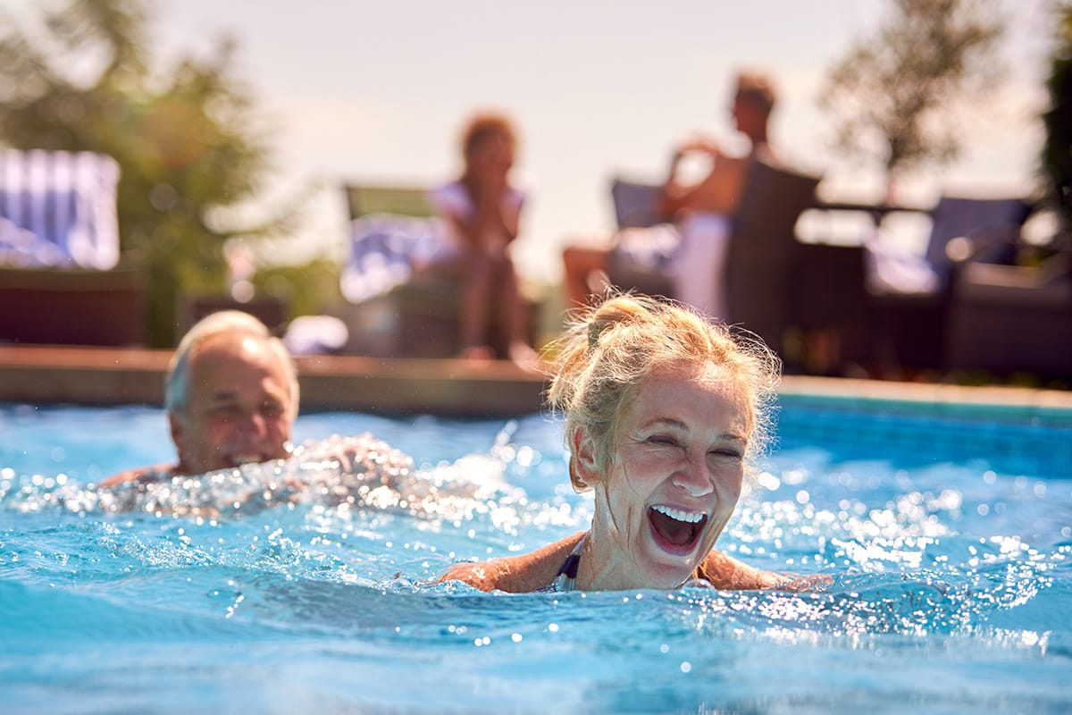 Two people laughing and swimming together in the backyard pool.