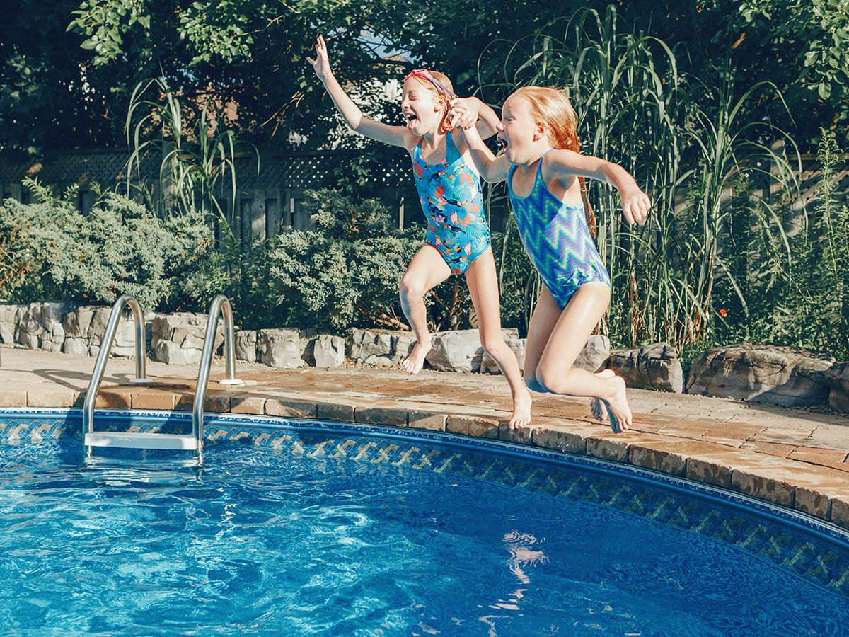 Two young girls jumping into a backyard in-ground pool holding hands.