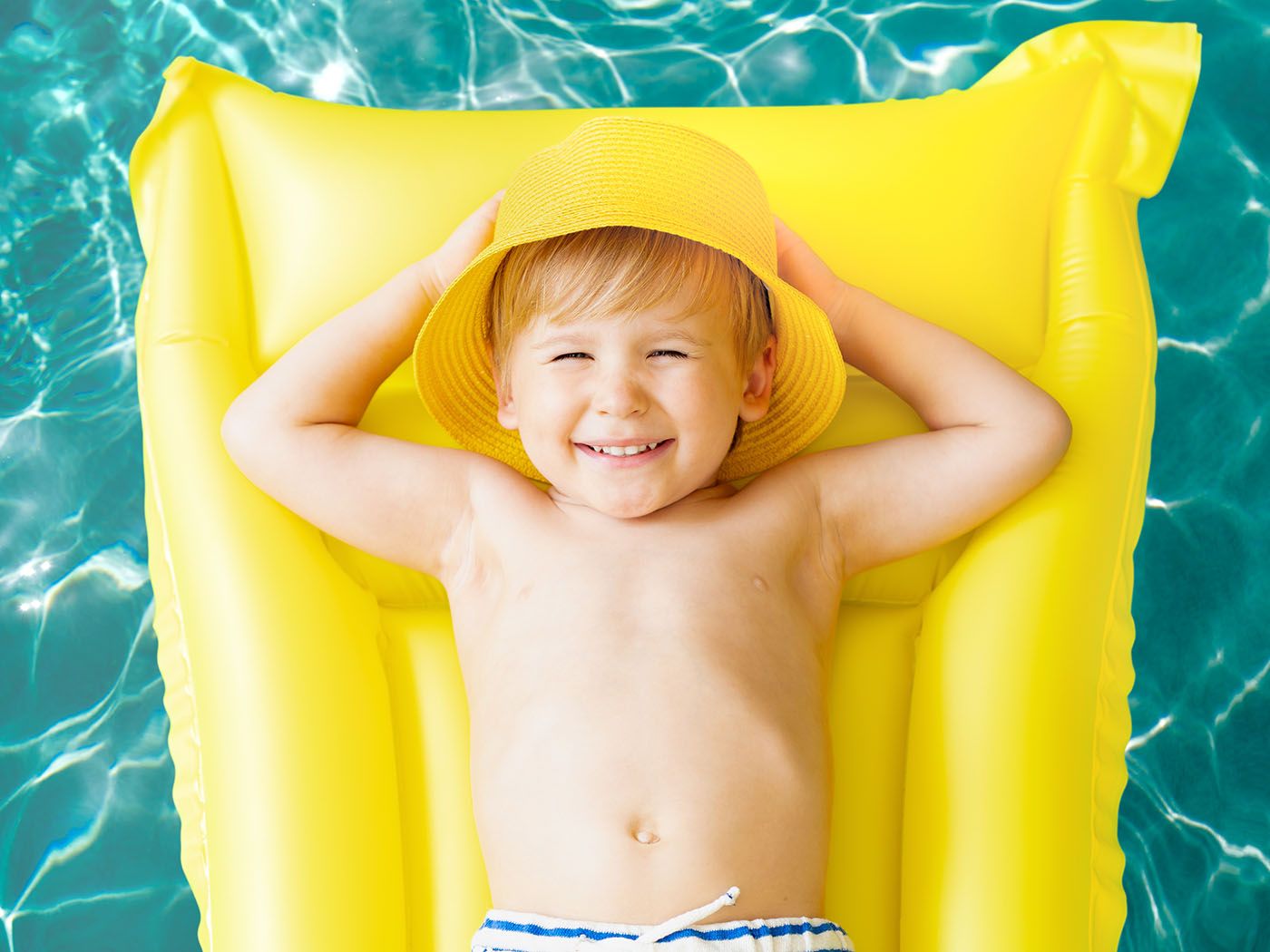 Young boy wearing a hat relaxing on a float in a fiberglass pool on a sunny day.