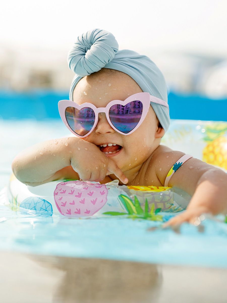 Baby with sunglasses resting on a float in a backyard swimmming pool.